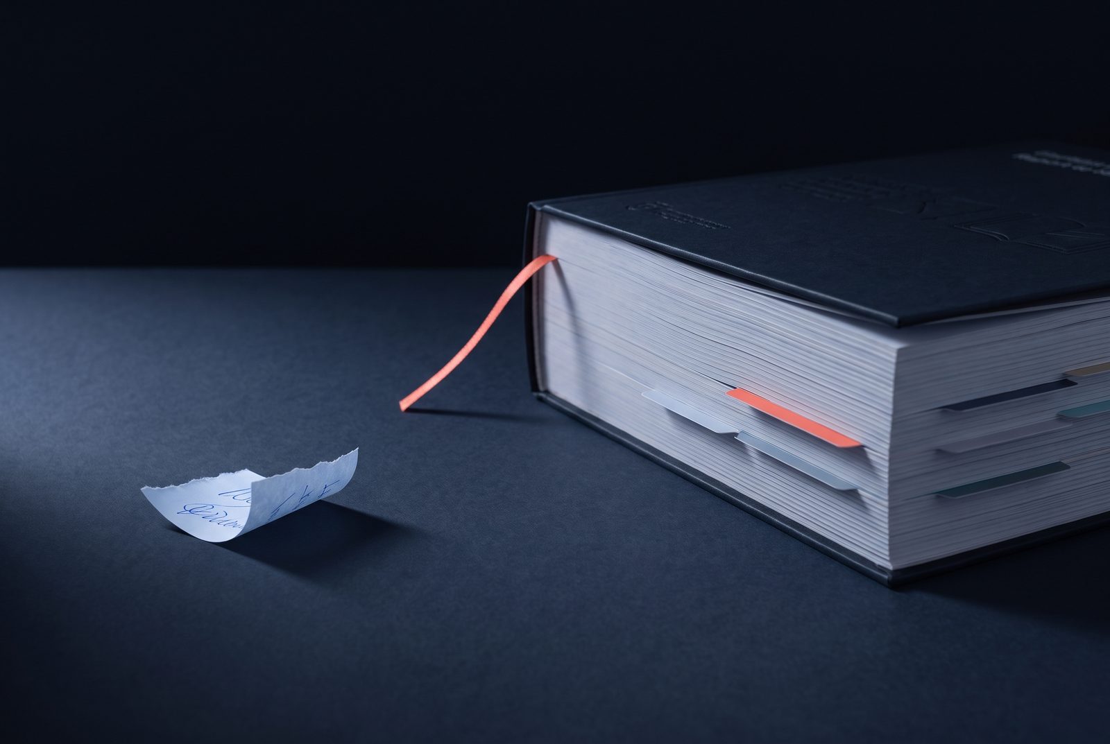 Un bout de papier portant un chiffre
        griffonné, posé à côté d'un dossier relié à onglets, nettement plus épais.